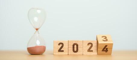 flipping block 2023 to 2024 text with hourglass on table. Resolution, time, plan, goal, motivation, reboot, countdown  and New Year holiday concepts photo