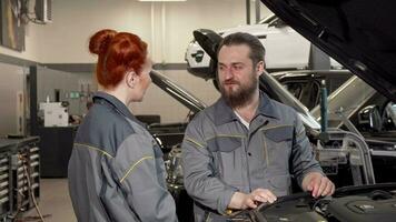 barbado mecánico hablando a su hembra colega a el automóvil taller video