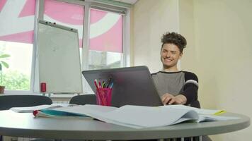 Young male college student smiling, typing on his laptop video