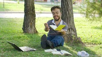 contento enano estudiante estudiando al aire libre. él es haciendo deberes en el parque. video