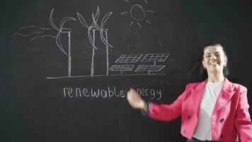 Woman writing Renewable Energy on blackboard smiling looking at camera. video