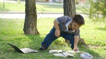 olycklig dvärg- studerande studerar utomhus. han är håller på med hans läxa i de parkera. video