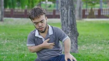 enano joven hombre con cofre dolor es en el parque. enano joven hombre con salud problema. video