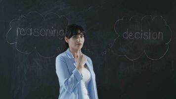 The woman writing Reasoning on the blackboard looks at the camera with a smile. video