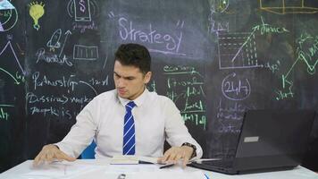 Businessman writes Strategy Implementation on blackboard and looks at projects. video