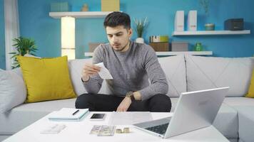 Frustrated man looking at bills doing calculations with calculator at home. video