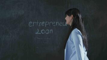 Frau Schreiben Unternehmer Darlehen auf Tafel sieht aus oben mit glücklich Ausdruck. video