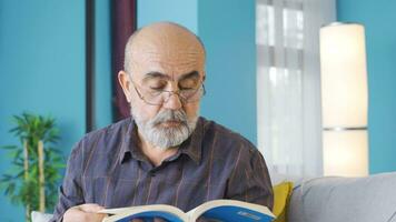 cultivé vieux homme en train de lire une livre à maison. video