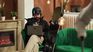 Male tourist works on laptop before starting skiing session down alpine slopes, searching for reviews and places at exclusive mountain resort. Equipped man using modern gadget. video