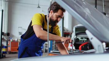 Licensed repairman in car service picks torque wrench from work station bench, using it to tighten bolts after replacing engine. Garage worker uses professional tools to fix client automobile video