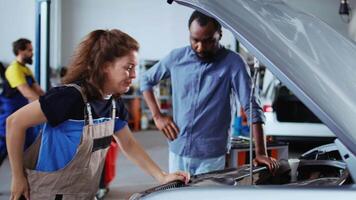 mecánico en garaje refinamiento fijación coche para cliente, mirando debajo vehículo capucha a eliminar restante petróleo fugas empleado haciendo rutina componentes limpieza en cliente automóvil en auto reparar tienda video