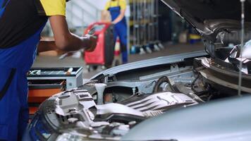 Trained engineer in car service uses torque wrench to tighten bolts inside vehicle after fixing components inside. African american repair shop expert utilizes professional tools to mend automobile video