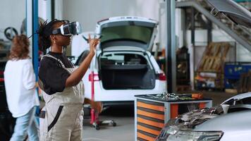 concesso in licenza ingegnere nel auto riparazione negozio utilizzando virtuale la realtà occhiali per visualizzare auto componenti nel ordine per fix loro. africano americano donna indossare moderno vr cuffia mentre Lavorando su danneggiato veicolo video