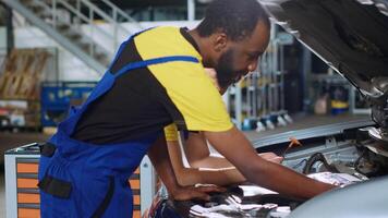 Qualified servicemen in auto repair shop working together on fixing car, discussing best options. Expert and colleague collaborating on servicing broken vehicle, checking for faulty components video