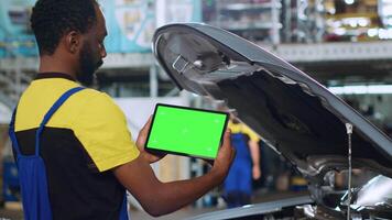 Mechanic using green screen tablet in car service to watch tutorial on how to fix unknown problem. Employee using chroma key device to look online for video showing how to repair broken vehicle part