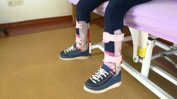 Child cerebral palsy disability with legs orthosis shoe sitting on hospital bed video