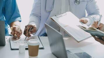 Multiracial medical team having a meeting with doctors in white lab coats and surgical scrubs seated at a table discussing a patients records video