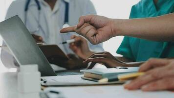 Multiracial medical team having a meeting with doctors in white lab coats and surgical scrubs seated at a table discussing a patients records video