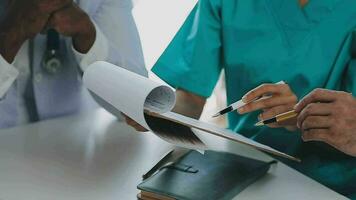 Multiracial medical team having a meeting with doctors in white lab coats and surgical scrubs seated at a table discussing a patients records video