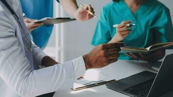 Multiracial medical team having a meeting with doctors in white lab coats and surgical scrubs seated at a table discussing a patients records video
