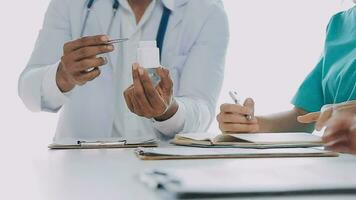Multiracial medical team having a meeting with doctors in white lab coats and surgical scrubs seated at a table discussing a patients records video