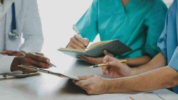 Multiracial medical team having a meeting with doctors in white lab coats and surgical scrubs seated at a table discussing a patients records video