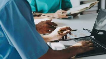 Multiracial medical team having a meeting with doctors in white lab coats and surgical scrubs seated at a table discussing a patients records video