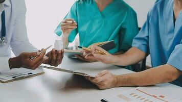 Multiracial medical team having a meeting with doctors in white lab coats and surgical scrubs seated at a table discussing a patients records video