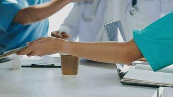 multiraciaal medisch team hebben een vergadering met artsen in wit laboratorium jassen en chirurgisch scrubs gezeten Bij een tafel bespreken een patiënten records video