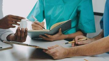 Multiracial medical team having a meeting with doctors in white lab coats and surgical scrubs seated at a table discussing a patients records video