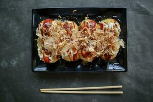 Takoyaki is a Japanese food, made from wheat flour dough, octopus meat, or other fillings, served with sauce, mayonnaise and topping in the form of katsuobushi or wood fish shavings. photo