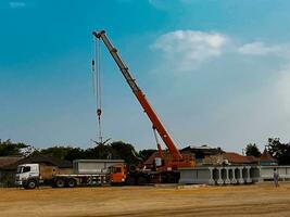 Mobile construction cranes with orange telescopic arms and big tower cranes in sunny day with white clouds and deep blue sky on background, heavy industry, is moving the load photo