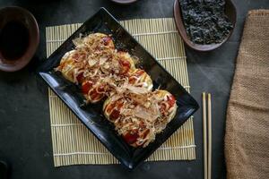 Takoyaki is a Japanese food, made from wheat flour dough, octopus meat, or other fillings, served with sauce, mayonnaise and topping in the form of katsuobushi or wood fish shavings. photo