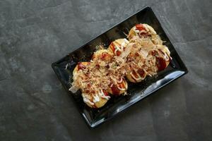 Takoyaki is a Japanese food, made from wheat flour dough, octopus meat, or other fillings, served with sauce, mayonnaise and topping in the form of katsuobushi or wood fish shavings. photo