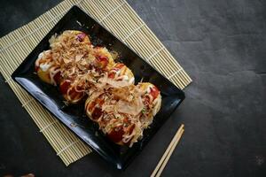 Takoyaki is a Japanese food, made from wheat flour dough, octopus meat, or other fillings, served with sauce, mayonnaise and topping in the form of katsuobushi or wood fish shavings. photo