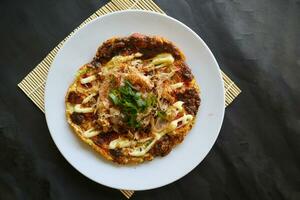 okonomiyaki, Traditional Japanese Pizza, Japanese hot plate pizza from Okonomiyaki. made of flour which is diluted with water or dashi, plus cabbage, chicken eggs, seafood and fried in a teppan photo