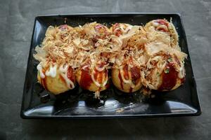 Takoyaki is a Japanese food, made from wheat flour dough, octopus meat, or other fillings, served with sauce, mayonnaise and topping in the form of katsuobushi or wood fish shavings. photo