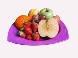 Strawberries, apples, oranges, grapes, pears served on a purple plate. Isolated white background photo