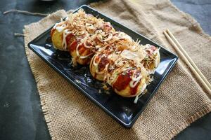 Takoyaki is a Japanese food, made from wheat flour dough, octopus meat, or other fillings, served with sauce, mayonnaise and topping in the form of katsuobushi or wood fish shavings. photo