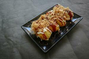 Takoyaki is a Japanese food, made from wheat flour dough, octopus meat, or other fillings, served with sauce, mayonnaise and topping in the form of katsuobushi or wood fish shavings. photo