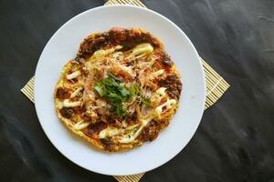 okonomiyaki, Traditional Japanese Pizza, Japanese hot plate pizza from Okonomiyaki. made of flour which is diluted with water or dashi, plus cabbage, chicken eggs, seafood and fried in a teppan photo