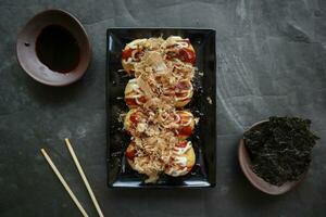 Takoyaki is a Japanese food, made from wheat flour dough, octopus meat, or other fillings, served with sauce, mayonnaise and topping in the form of katsuobushi or wood fish shavings. photo