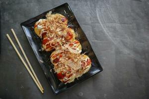Takoyaki is a Japanese food, made from wheat flour dough, octopus meat, or other fillings, served with sauce, mayonnaise and topping in the form of katsuobushi or wood fish shavings. photo