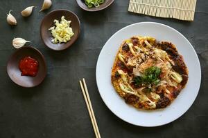 okonomiyaki, Traditional Japanese Pizza, Japanese hot plate pizza from Okonomiyaki. made of flour which is diluted with water or dashi, plus cabbage, chicken eggs, seafood and fried in a teppan photo