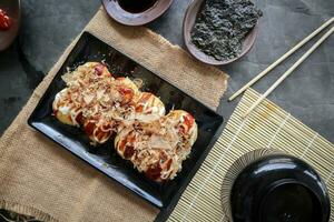 Takoyaki is a Japanese food, made from wheat flour dough, octopus meat, or other fillings, served with sauce, mayonnaise and topping in the form of katsuobushi or wood fish shavings. photo