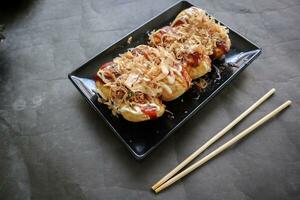 Takoyaki is a Japanese food, made from wheat flour dough, octopus meat, or other fillings, served with sauce, mayonnaise and topping in the form of katsuobushi or wood fish shavings. photo