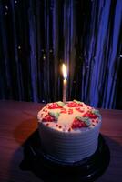 cumpleaños pastel con asperja fresa y uno velas en un azul antecedentes foto