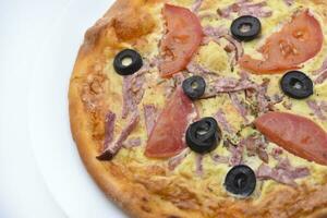 Meat round pizza with olives on a white plate. Italian flatbread. photo