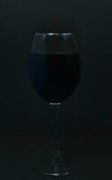 Glass wine glass on a black background. Red wine in a dark room. photo