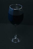 Glass wine glass on a black background. Red wine in a dark room. photo